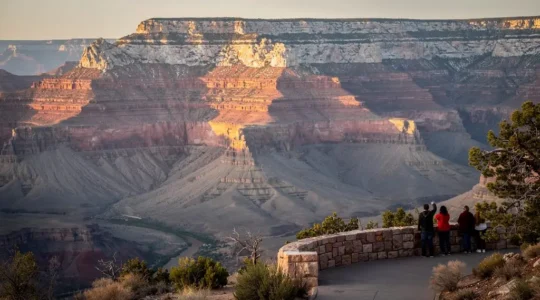 Vue panoramique depuis un belvédère du Grand Canyon montrant les strates rocheuses colorées et des visiteurs observant les couches géologiques