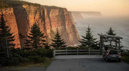 Panorama d'une falaise côtière de l'Atlantique canadien vue depuis un belvédère routier avec parement de bois et voiture garée au bord de la route.