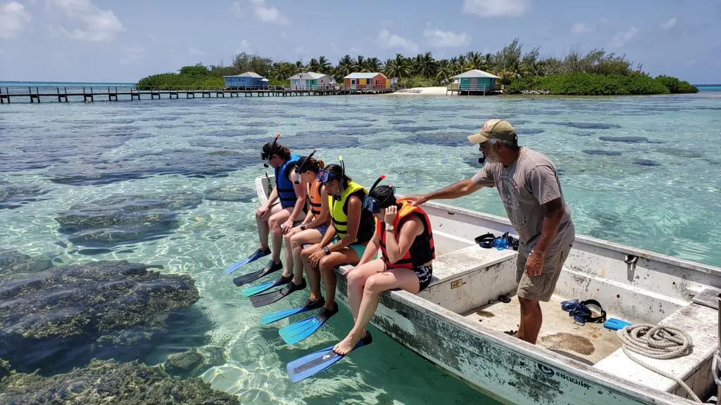 Un guide local briefe un petit groupe de snorkelers équipés de gilets et de masques à bord d'un bateau amarré près d'un récif peu profond aux eaux turquoise