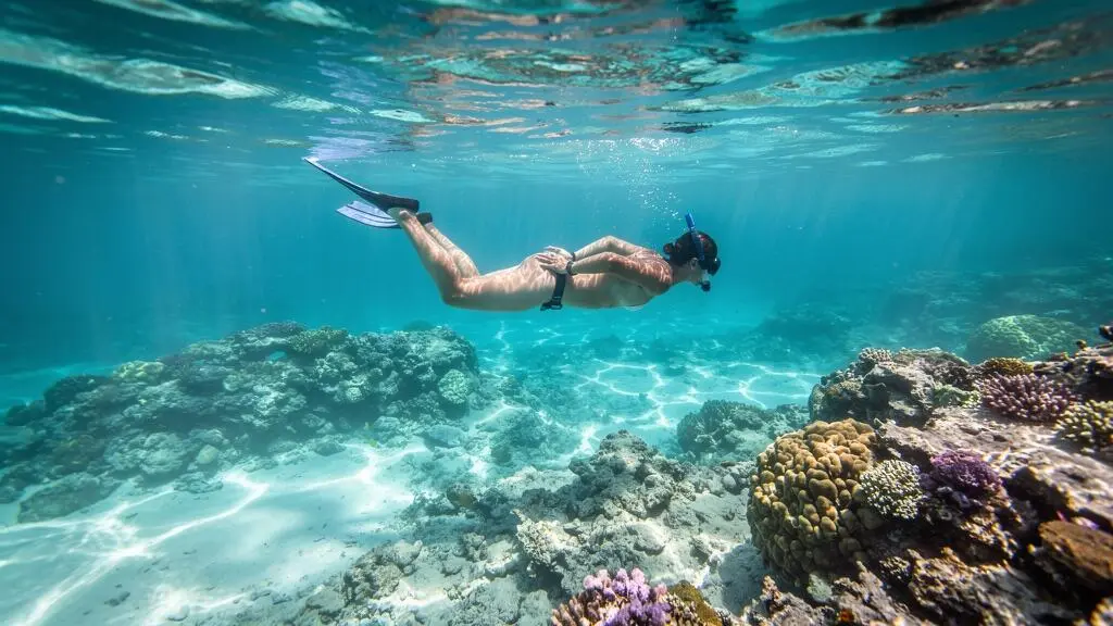 Un nageur en masque et tuba flotte horizontalement à la surface, au-dessus d'un récif corallien caribéen peu profond, sans toucher les coraux.