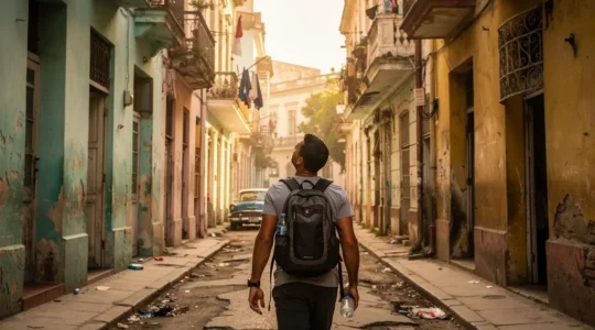 Un voyageur à pied marche dans une rue de la Vieille Havane bordée de façades coloniales patinées, en fin d'après-midi.
